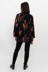 Back view of woman wearing a black top with vivid leaf designs and relaxed fit bell sleeves