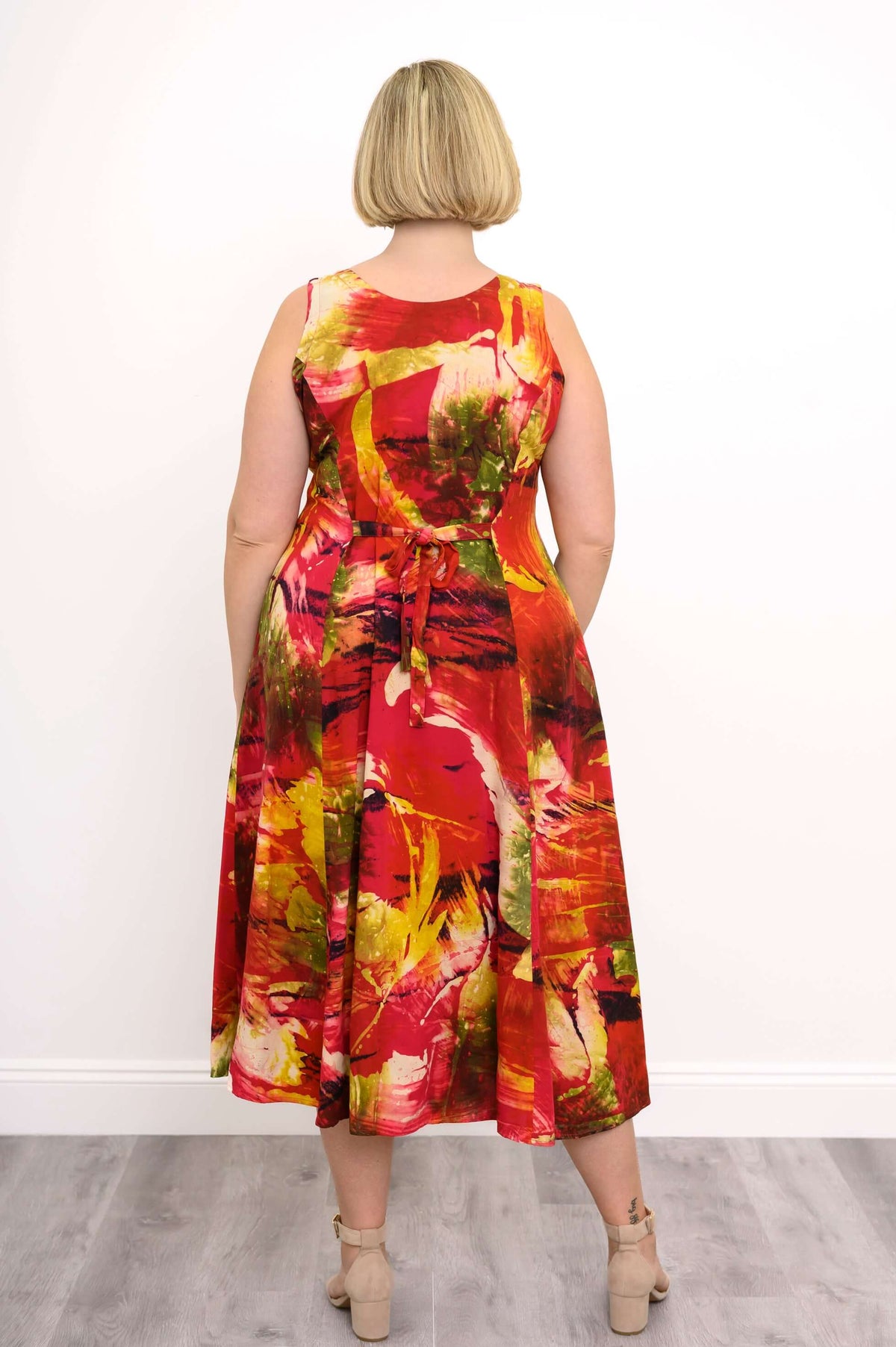 Back view of woman in a sleeveless, tie-back midi dress with red, yellow, and green abstract patterns