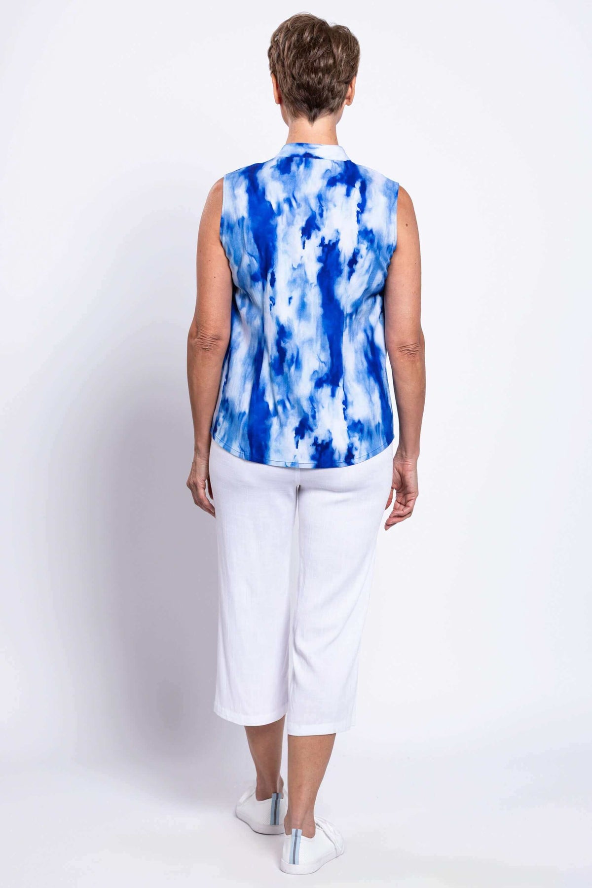 Back view of a woman wearing a blue tie-dye sleeveless blouse and white pants