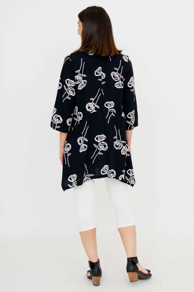 Back view of woman wearing black tunic with white rose sketches and white leggings