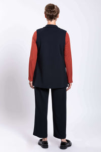 Back view of model in black open vest, matching pants, and rust colored long sleeve shirt