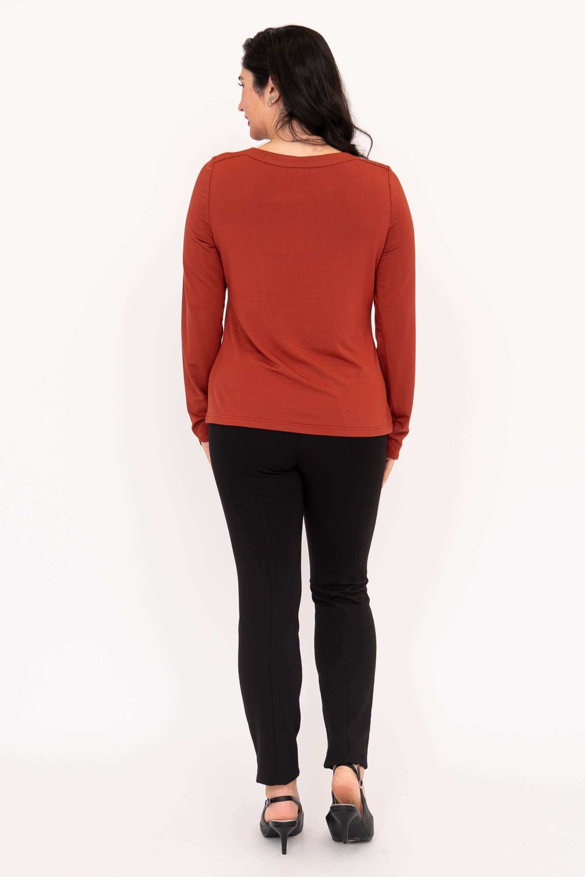 Back view of model wearing rust-colored Mona boat neck long sleeve top and black pants