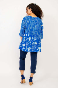 Back view of woman wearing blue batik Palace Blouse with flowy silhouette and navy crop pants