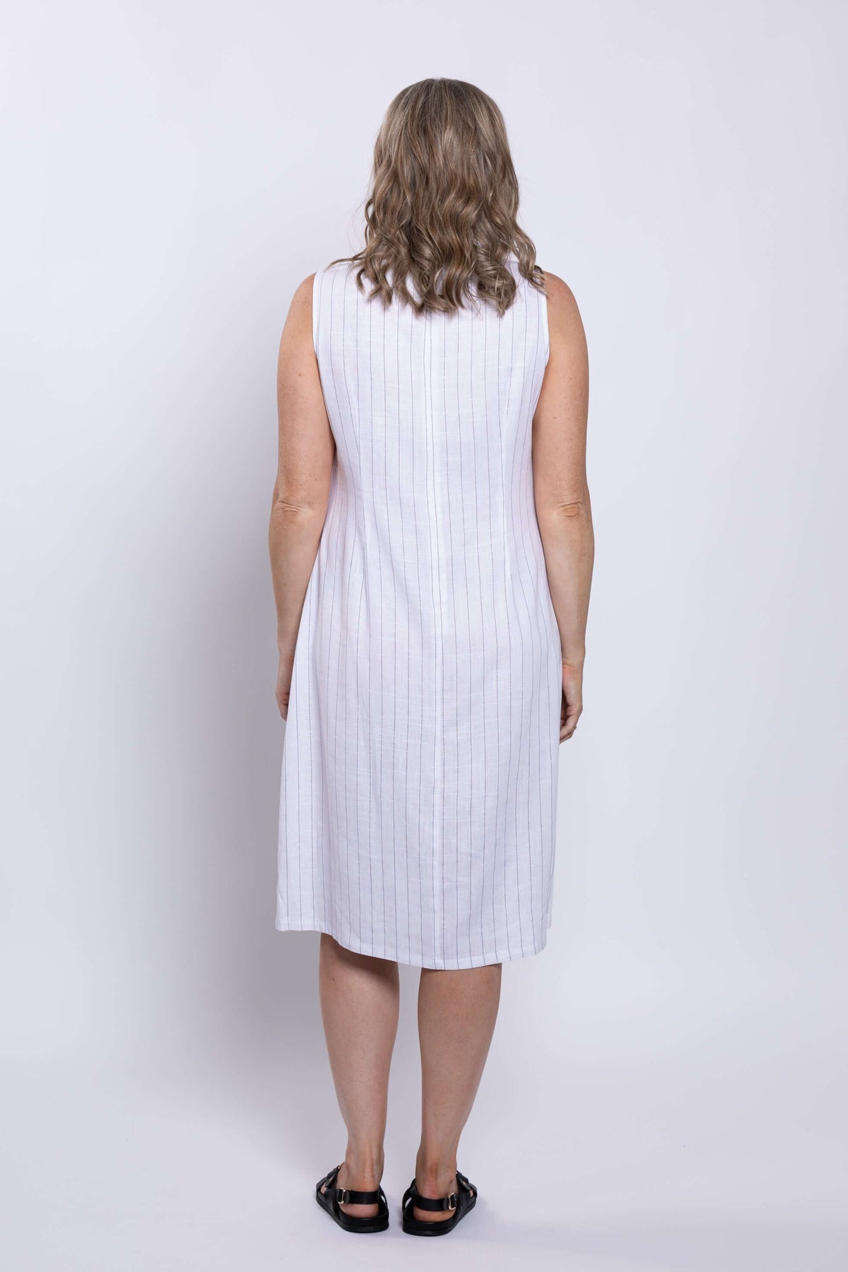 Back view of a woman in a white sleeveless dress with vertical stripes and black sandals
