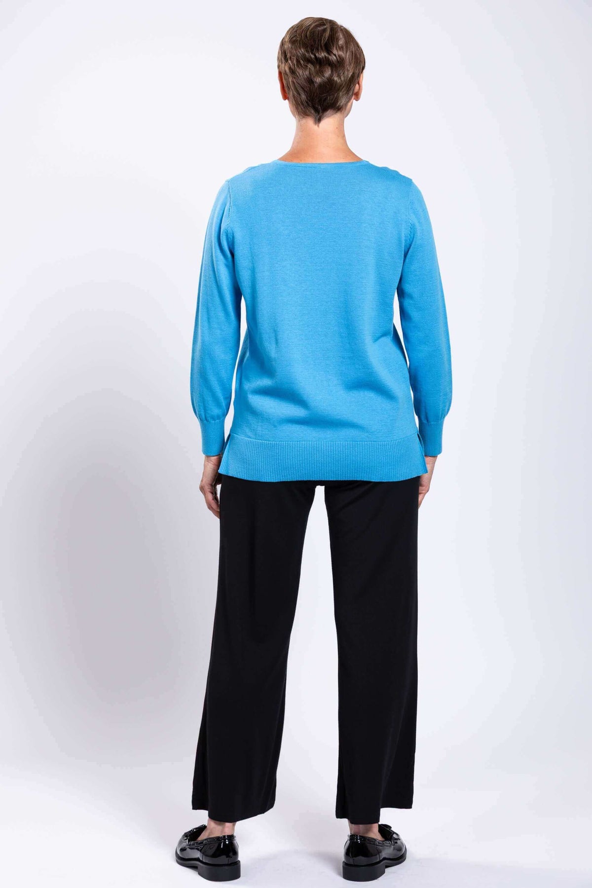 Back view of a woman wearing a blue sweater with ribbed hem and black wide-leg pants