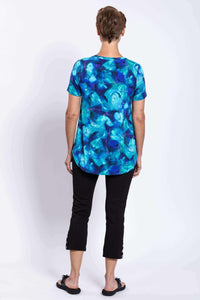 Woman modeling blue floral V-neck top with black cropped pants, back view