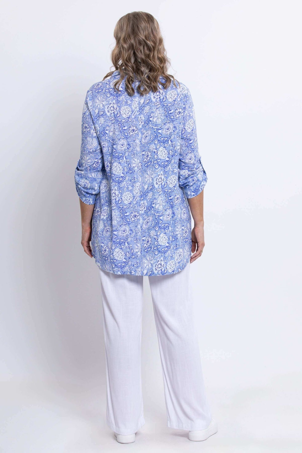 Back view of woman wearing blue paisley tunic with rolled sleeves and white pants