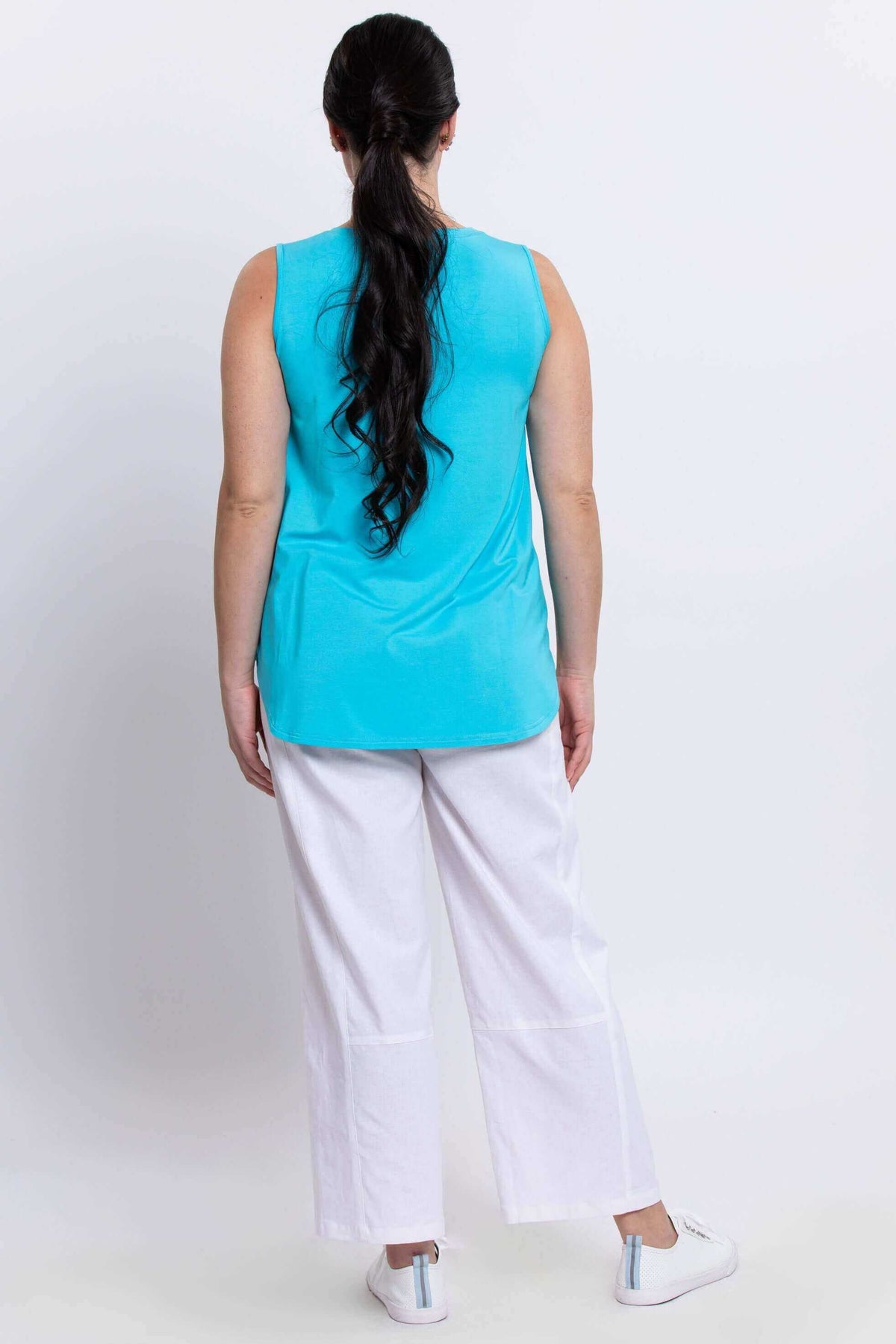 Back view of a woman wearing an aqua sleeveless tank top and white pants