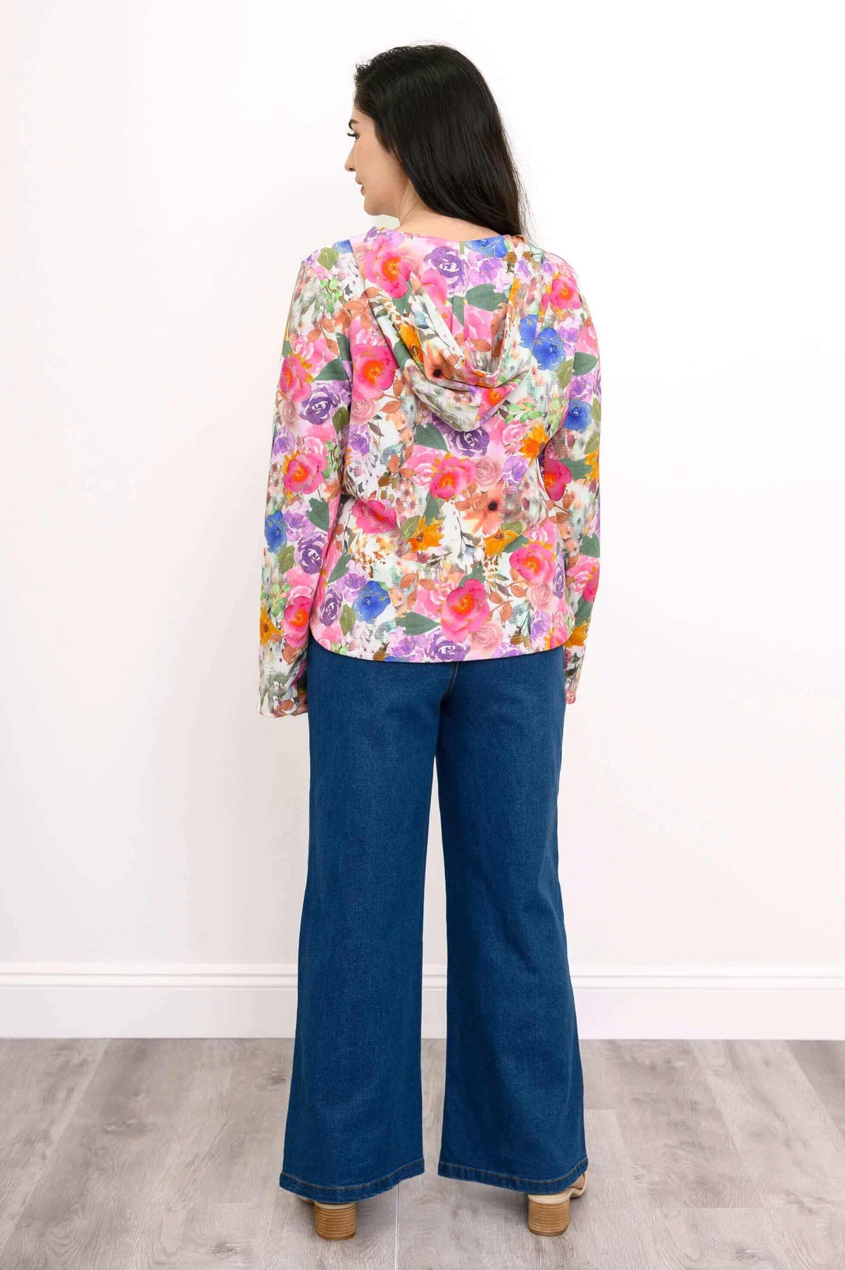 Back view of a woman wearing a vivid pink floral hoodie with a relaxed hood, blue jeans