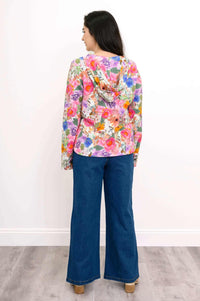 Back view of a woman wearing a vivid pink floral hoodie with a relaxed hood, blue jeans