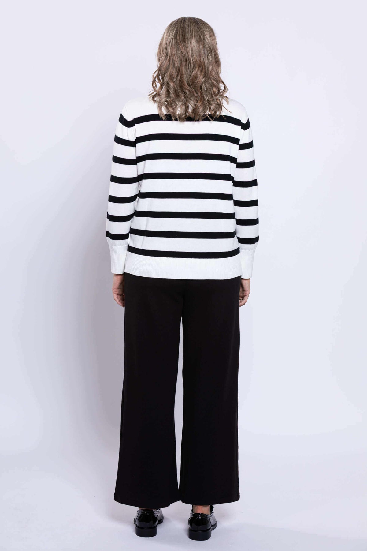 Back view of a woman in a black and tan Breton stripe V-neck sweater with black pants