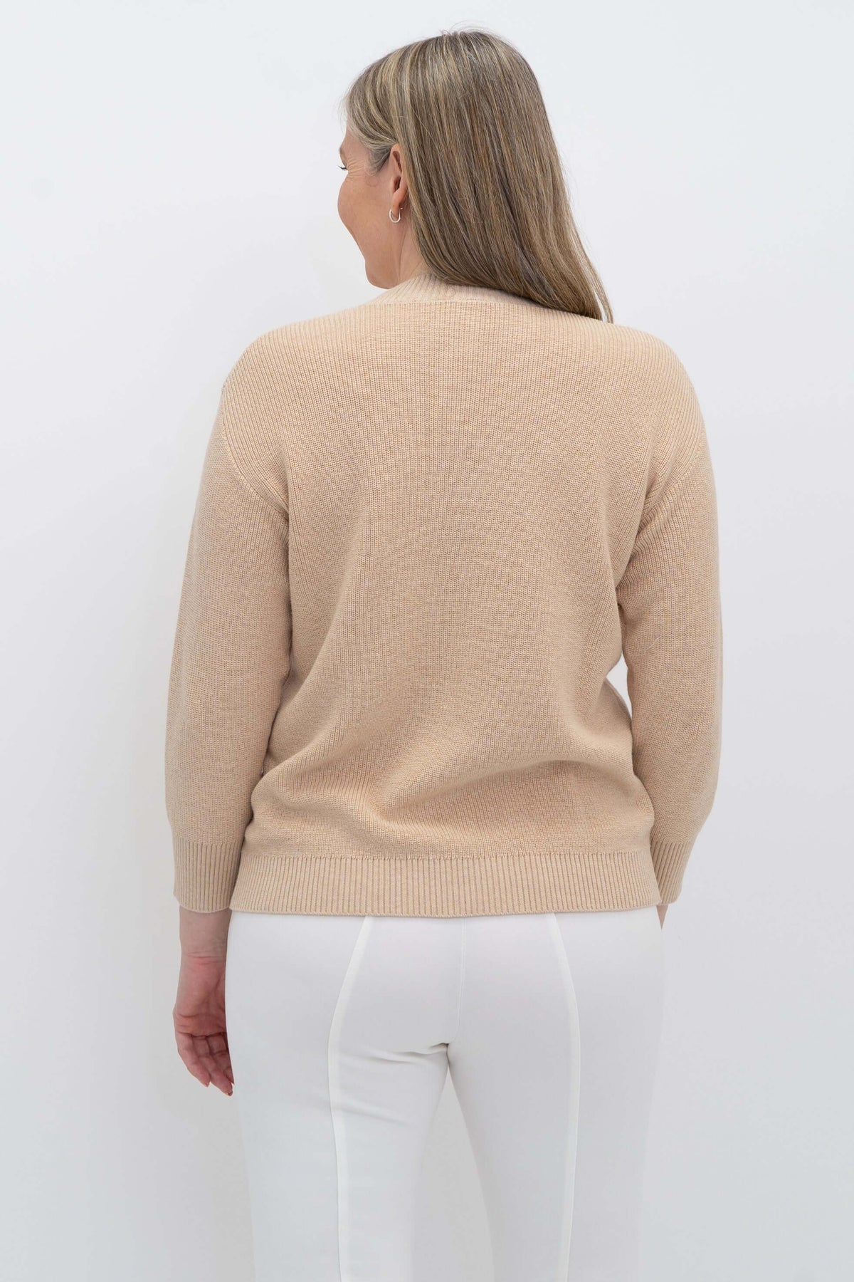 Back view of woman wearing a beige crew neck sweater and white pants