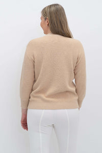 Back view of woman wearing a beige crew neck sweater and white pants