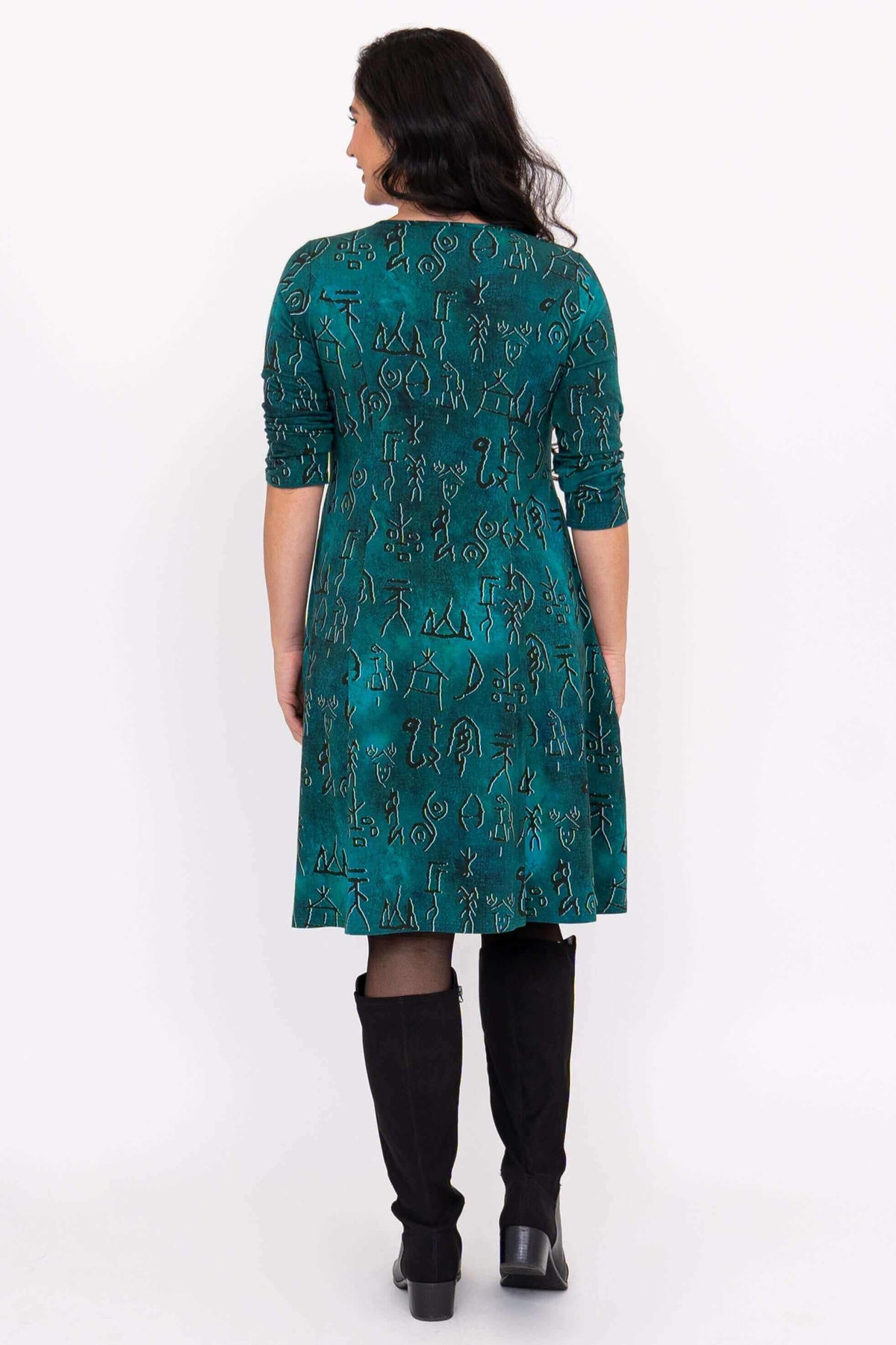 Back view of woman wearing a teal dress with petroglyph pattern and black boots