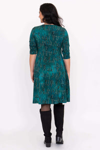 Back view of woman wearing a teal dress with petroglyph pattern and black boots