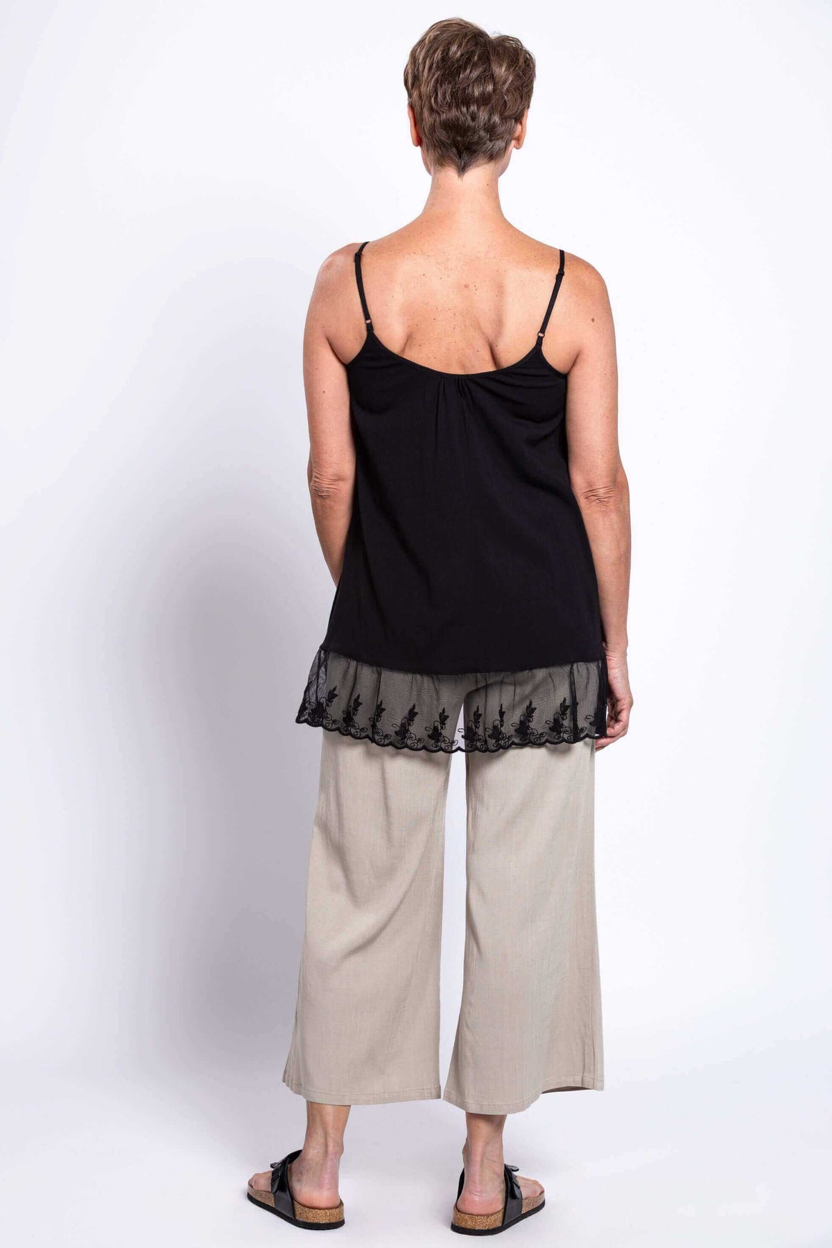 Back view of a woman in a black tank top with lace trim and beige pants