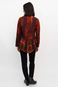 Back view of a woman in a colorful smocked tunic blouse with red and yellow leaf design