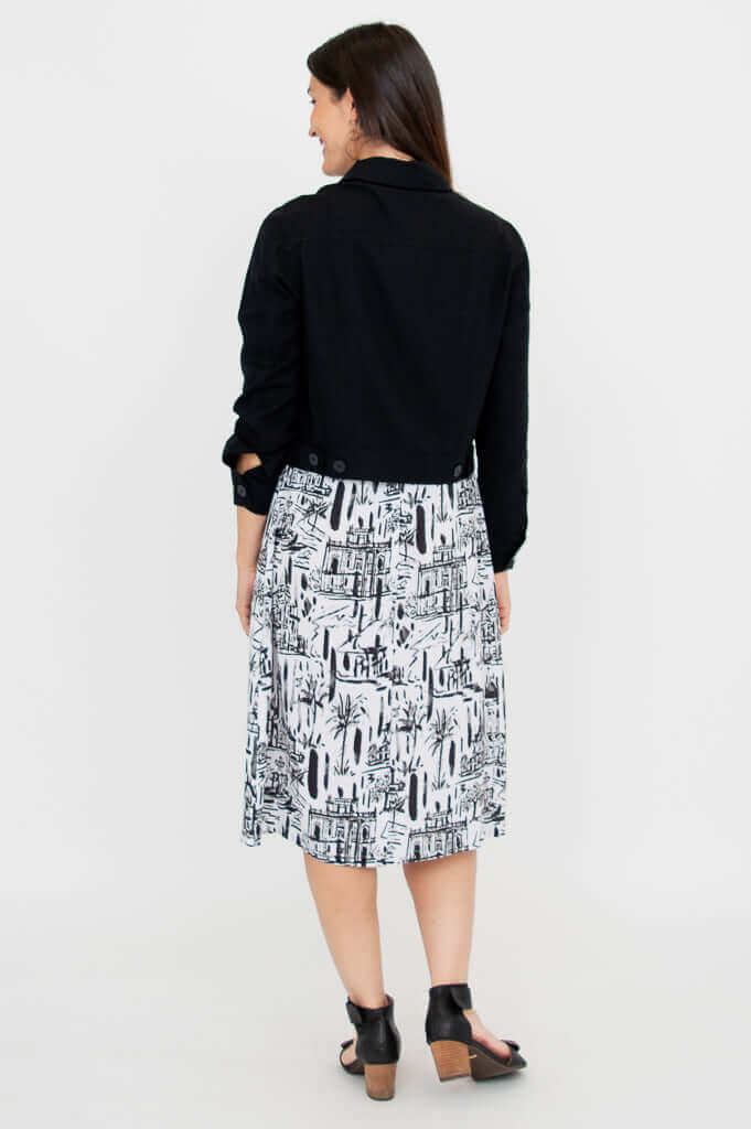 Back view of a woman modeling a black cropped jacket and a white cityscape print dress
