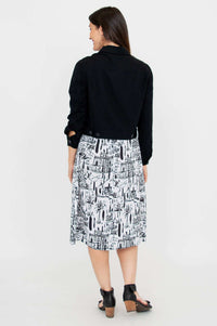 Back view of a woman modeling a black cropped jacket and a white cityscape print dress