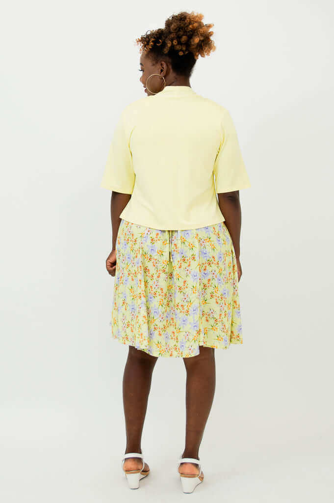 Back view of woman wearing a cropped light yellow jacket and floral dress