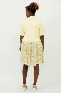 Back view of woman wearing a cropped light yellow jacket and floral dress