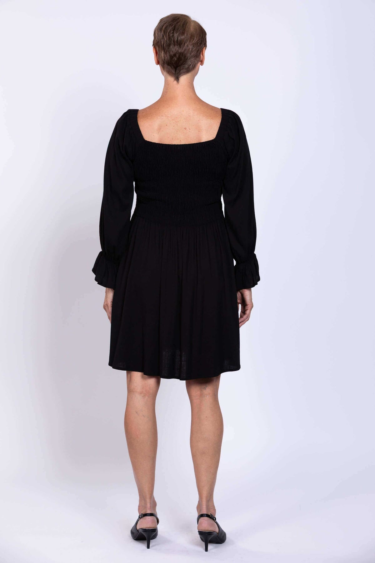 Back view of a woman wearing a black dress with a square neckline and shirred bodice