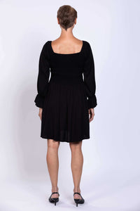 Back view of a woman wearing a black dress with a square neckline and shirred bodice