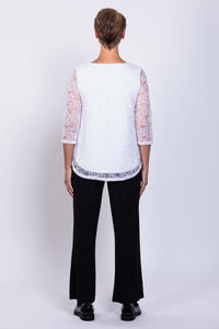 Back view of a woman wearing a white lace overlay top with 3/4 sleeves and black pants