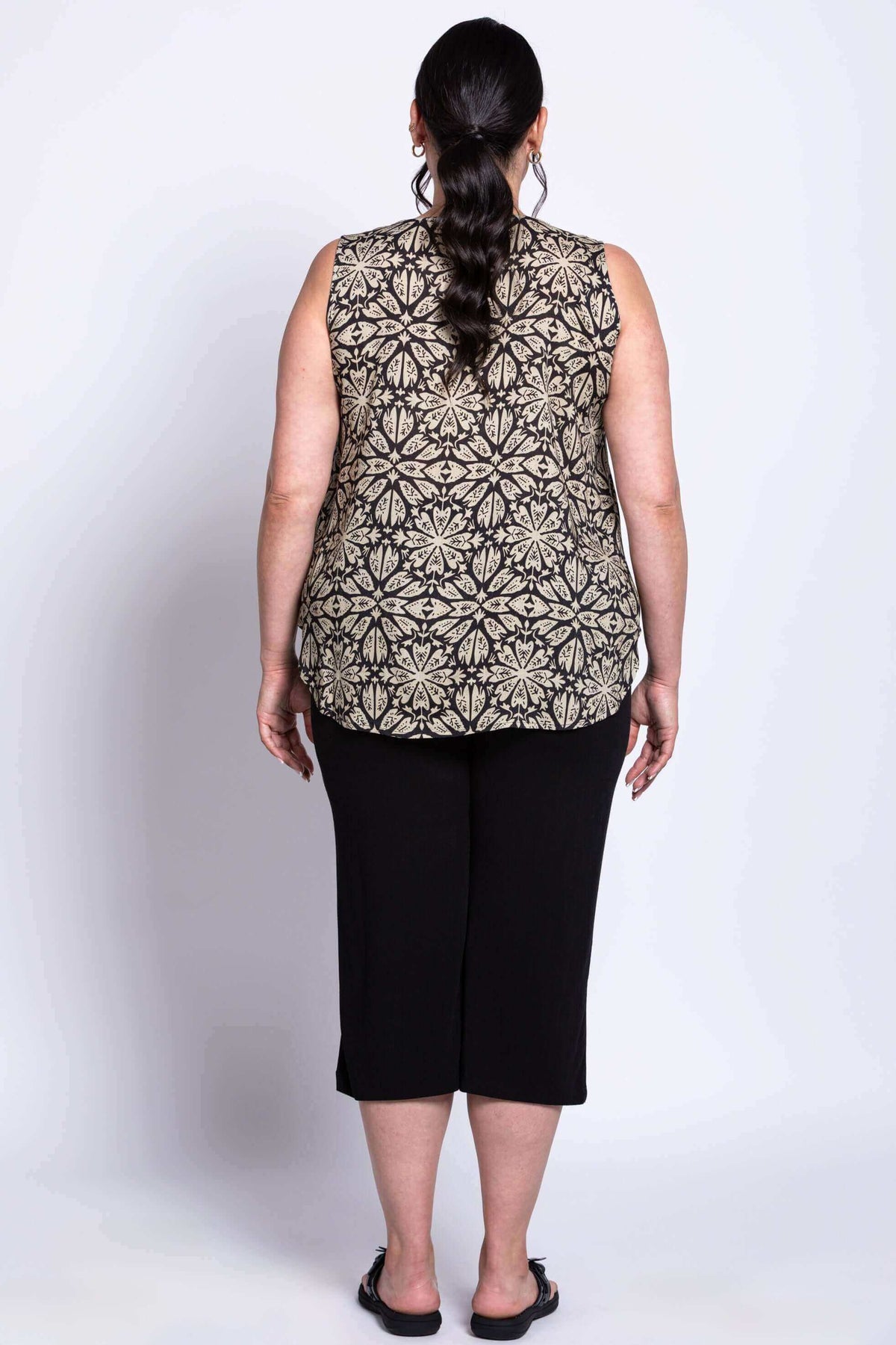full body back view of woman wearing black and beige print top, black capri pants, and black shoes