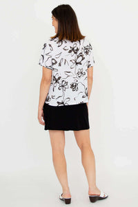 Back view of woman wearing a white floral print short-sleeve top and black skirt