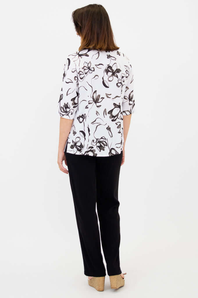 Rear view of woman in white blouse with black floral pattern and black pants