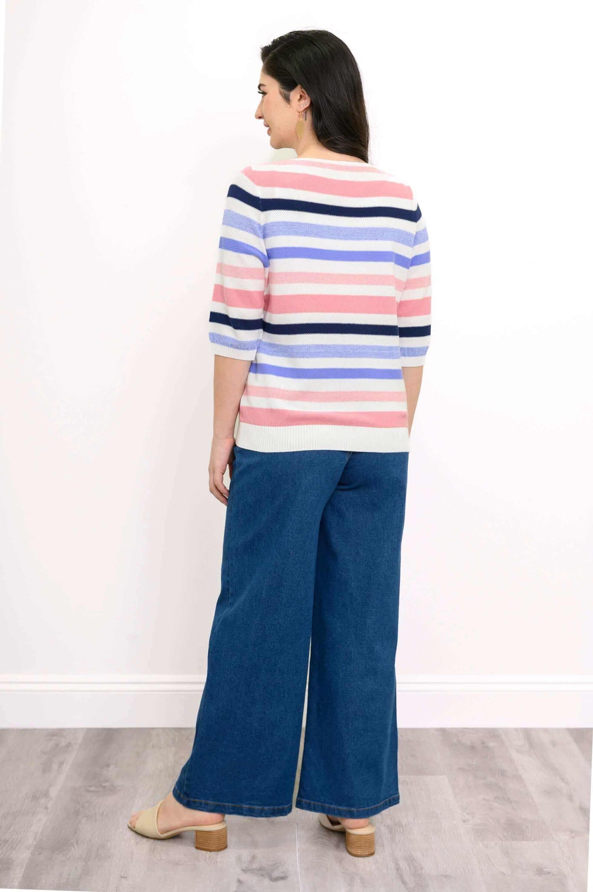Back view of a woman wearing a striped sweater in pastel and navy colors with blue jeans