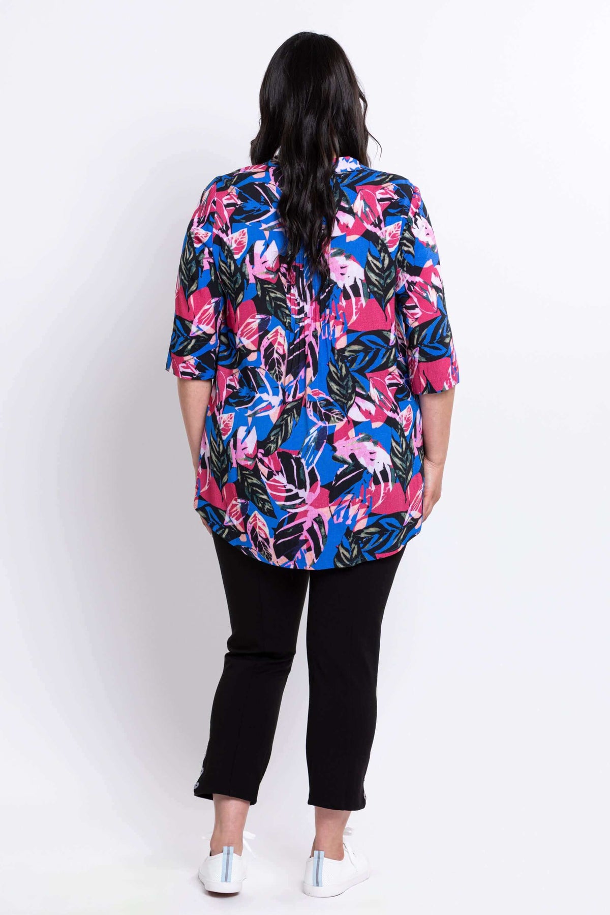 Full body back view of woman wearing blue and pink tropical print top and black pants