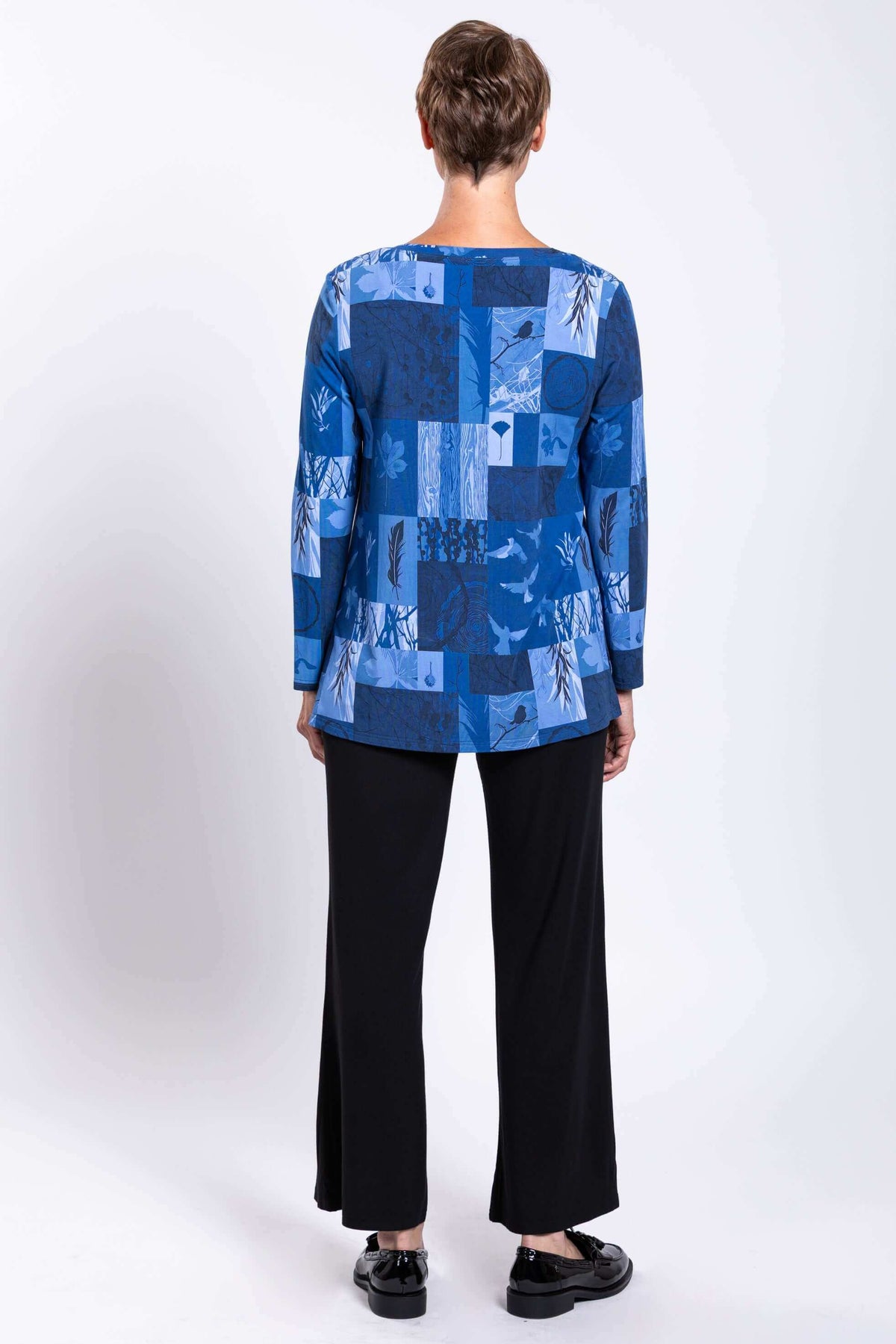 Back view of blue patchwork long-sleeve top worn by a woman with black pants