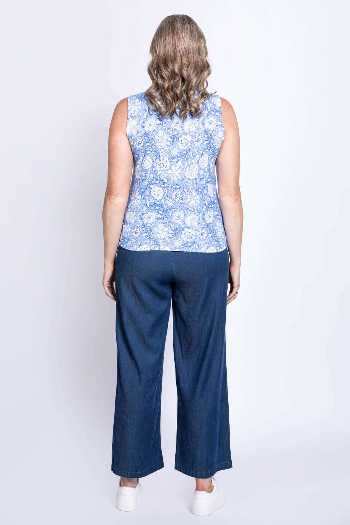 Back view of a woman wearing a blue floral tank top and denim pants