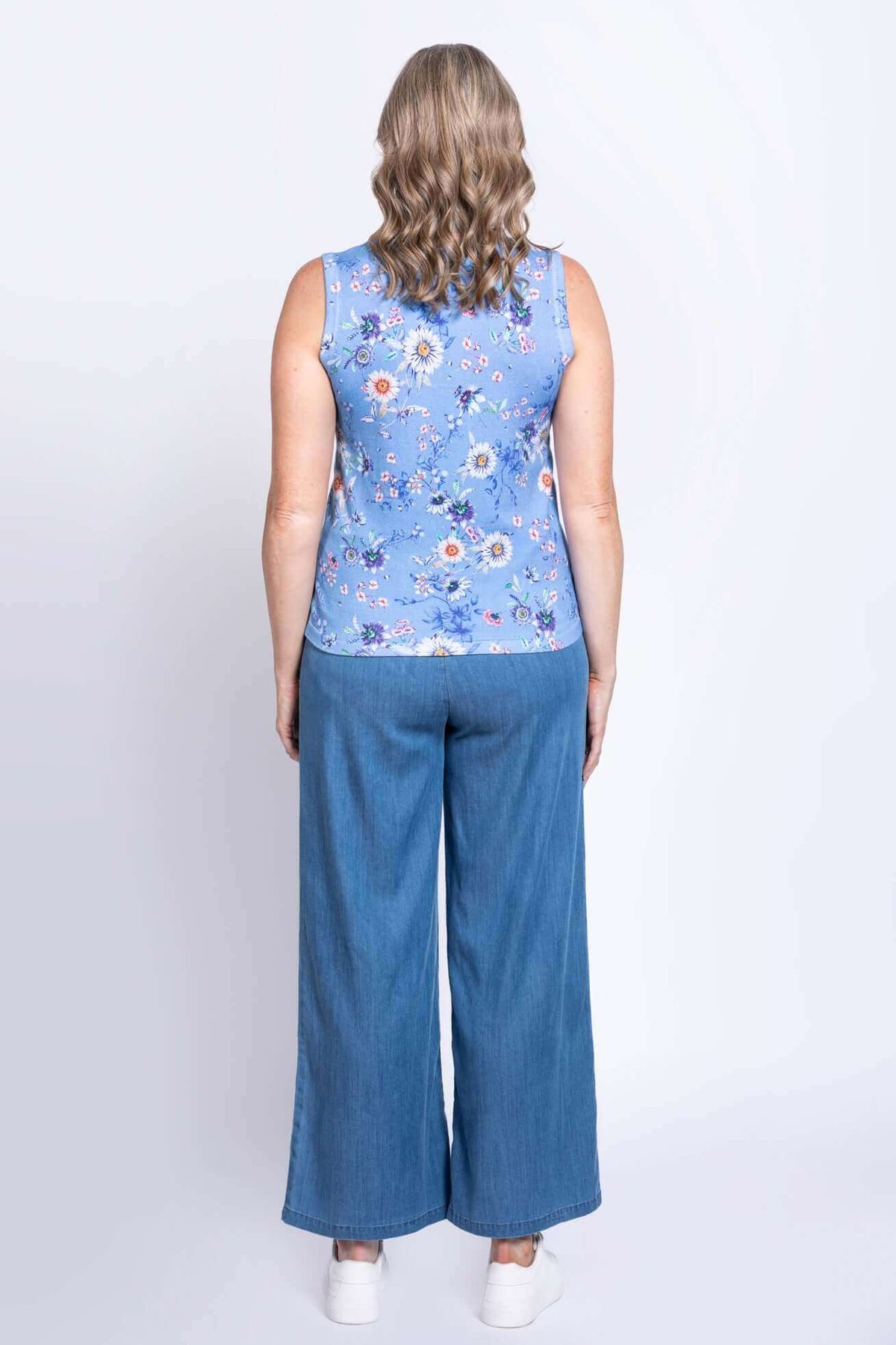 Back view of woman in blue floral cotton tank top and blue denim pants