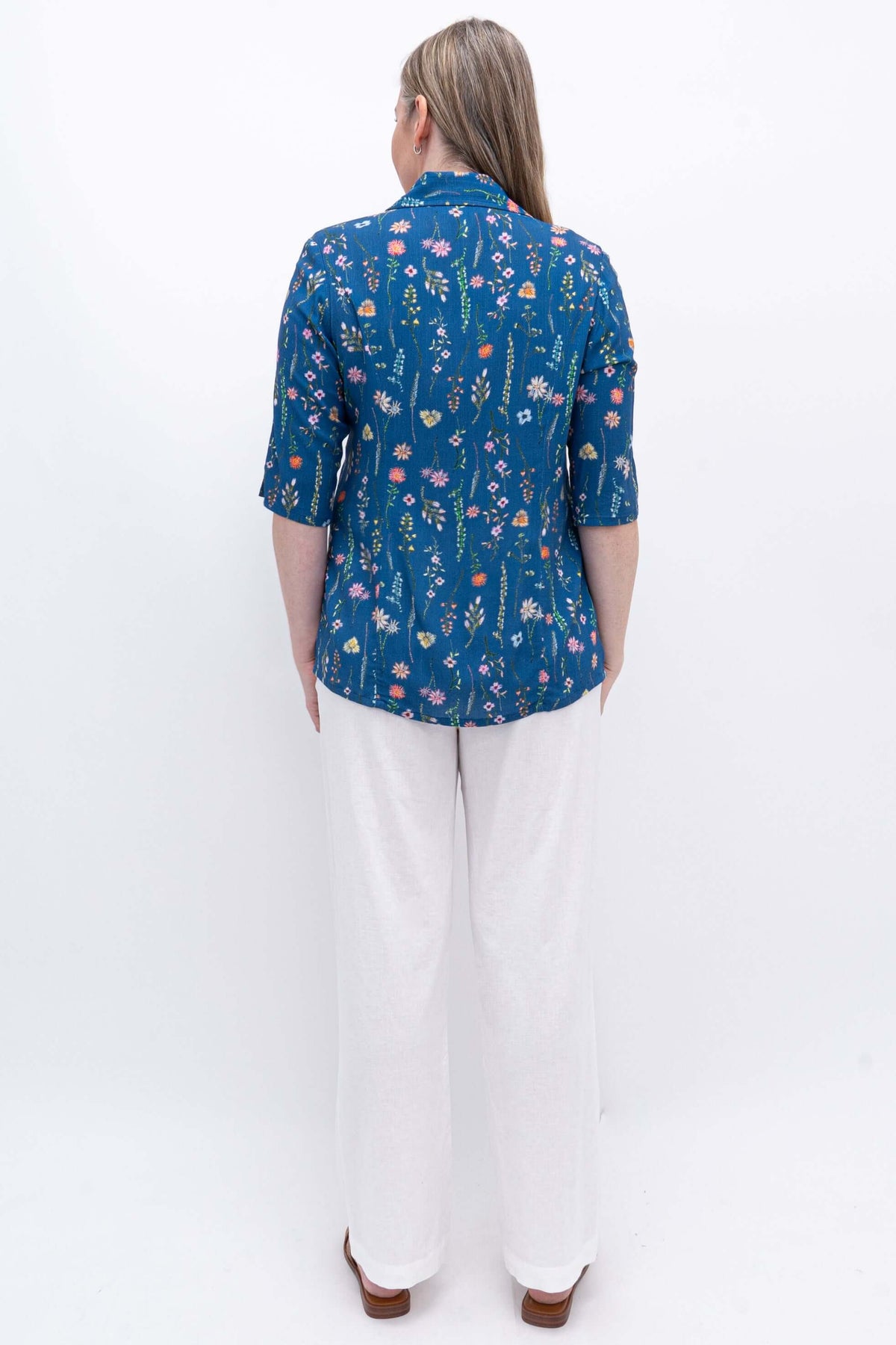 Back view of model wearing blue floral print top and straight leg white trousers against a white background