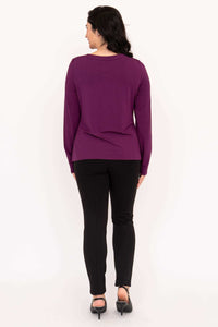 Back view of a woman in a purple long sleeve boat neck top and black pants