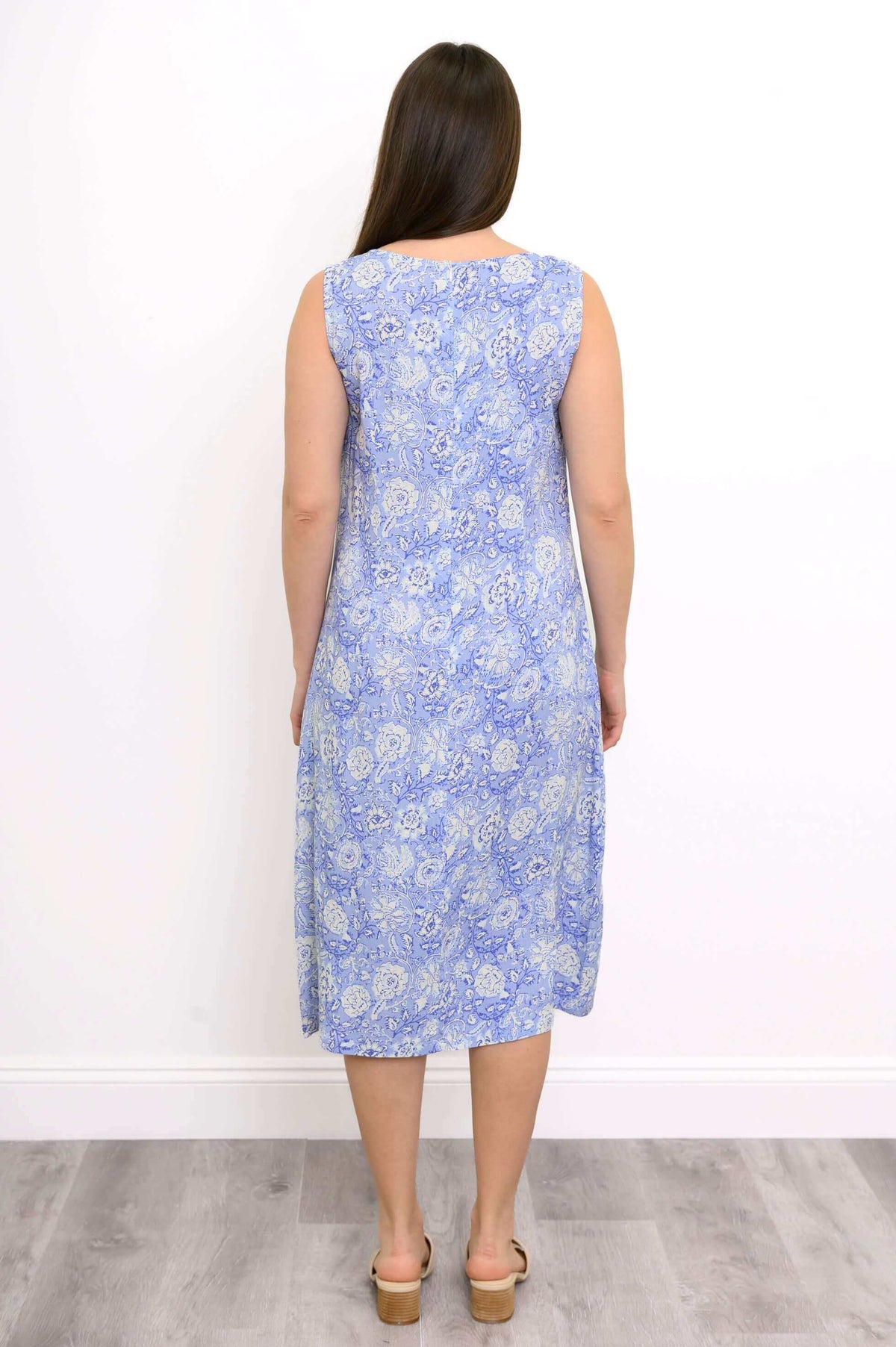 Back view of woman wearing sleeveless long blue and white floral print dress and sandals