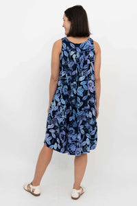 Back view of a woman in a navy blue sleeveless floral dress with pleats and pockets
