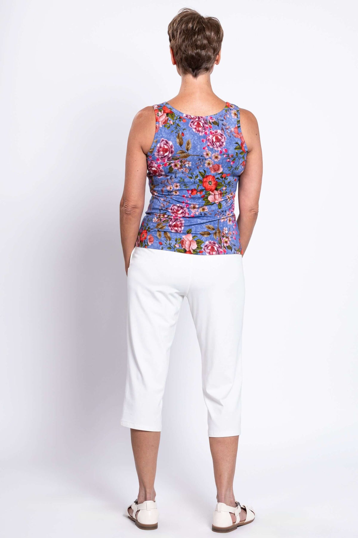 Back view of woman wearing blue floral reversible bamboo tank top with white pants