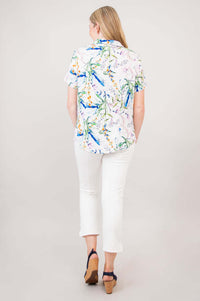 Back view of a woman in a floral button-up shirt paired with white pants and navy wedges