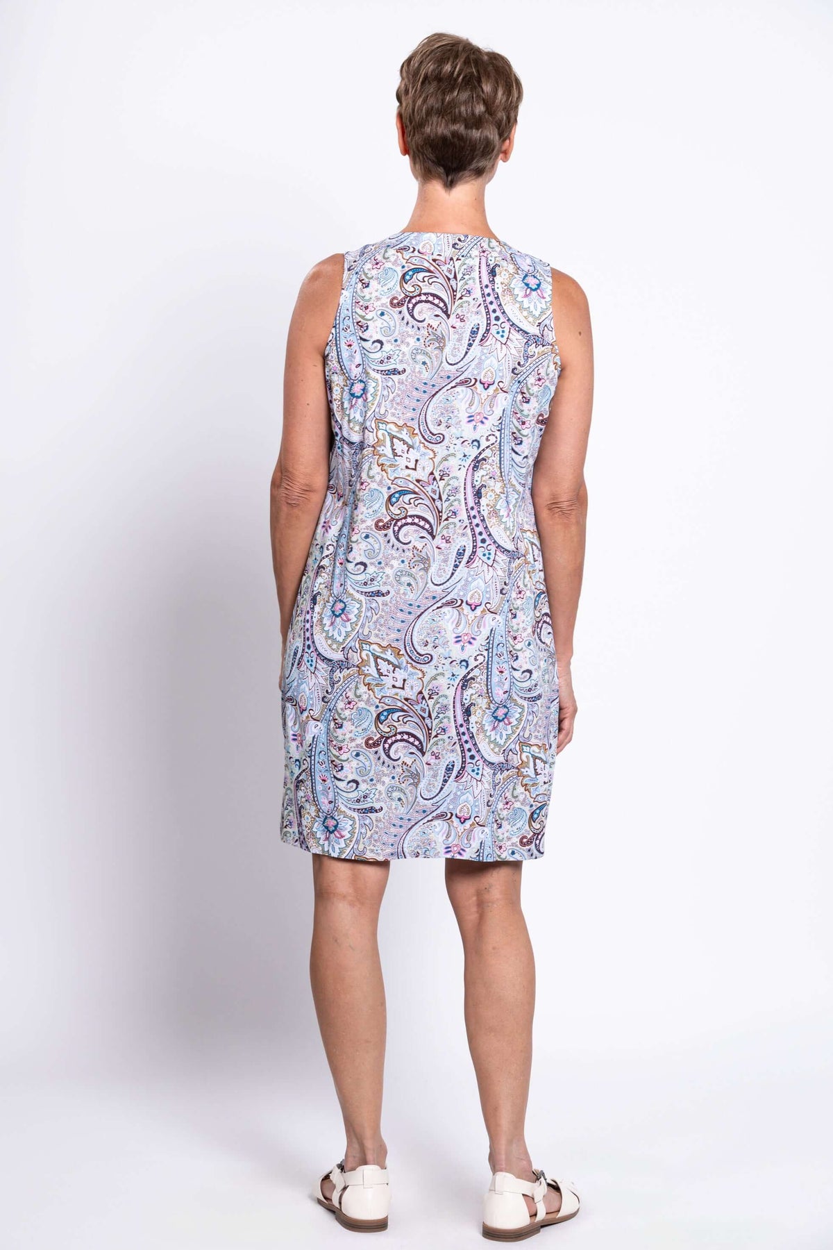 Back view of woman in sleeveless paisley print dress against a white background