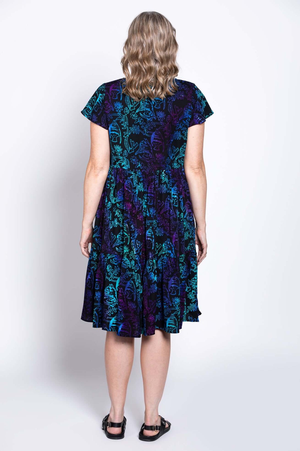 Woman wearing a black dress with blue and purple print, back view showing tiered skirt