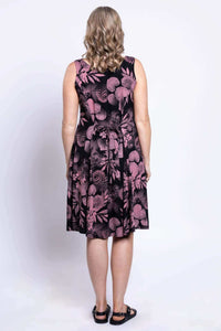 Back view of a woman in a sleeveless black A-line dress with pink floral print and tie belt