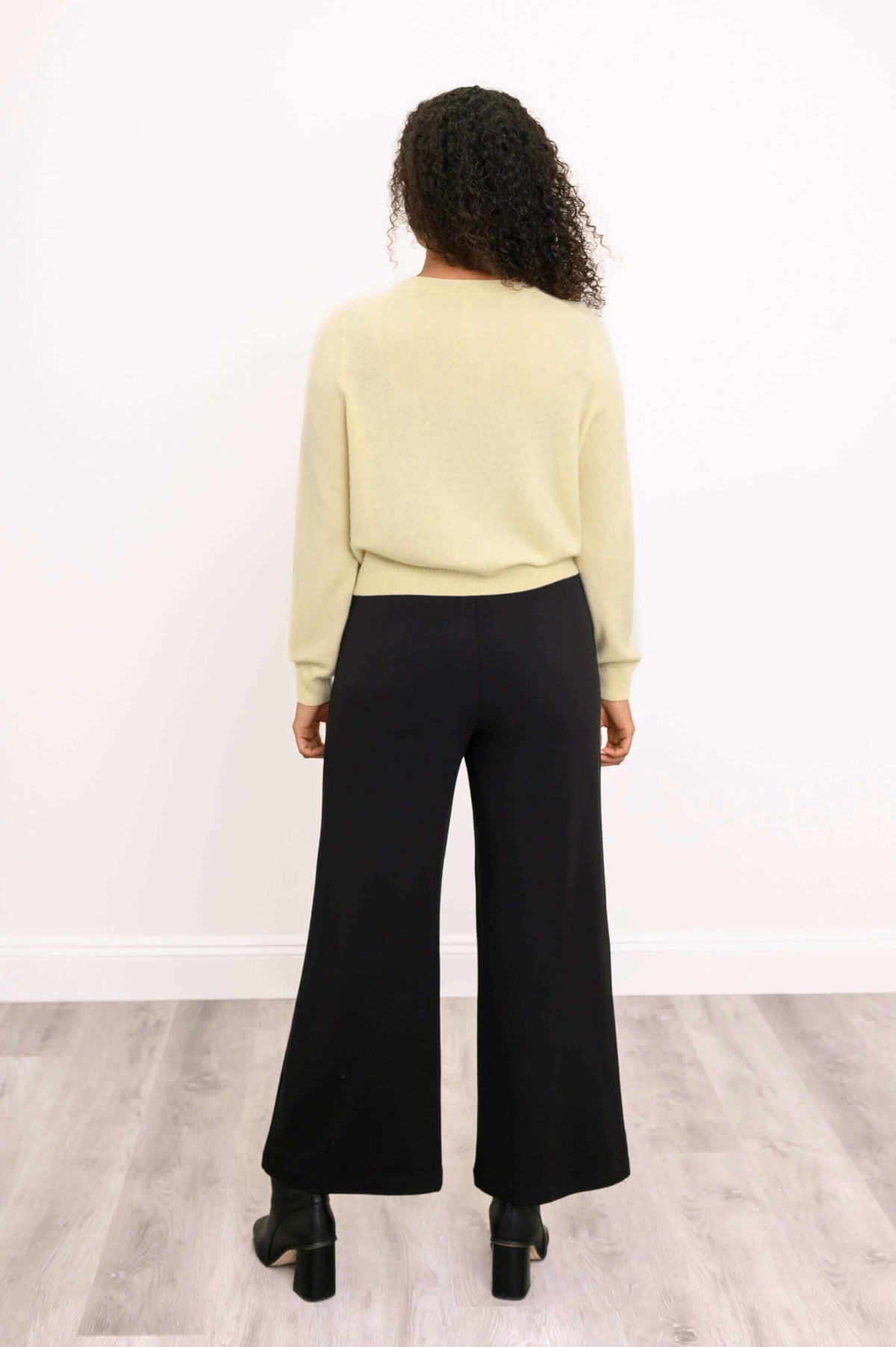 Back view of a woman in a light yellow cardigan and black wide-leg pants