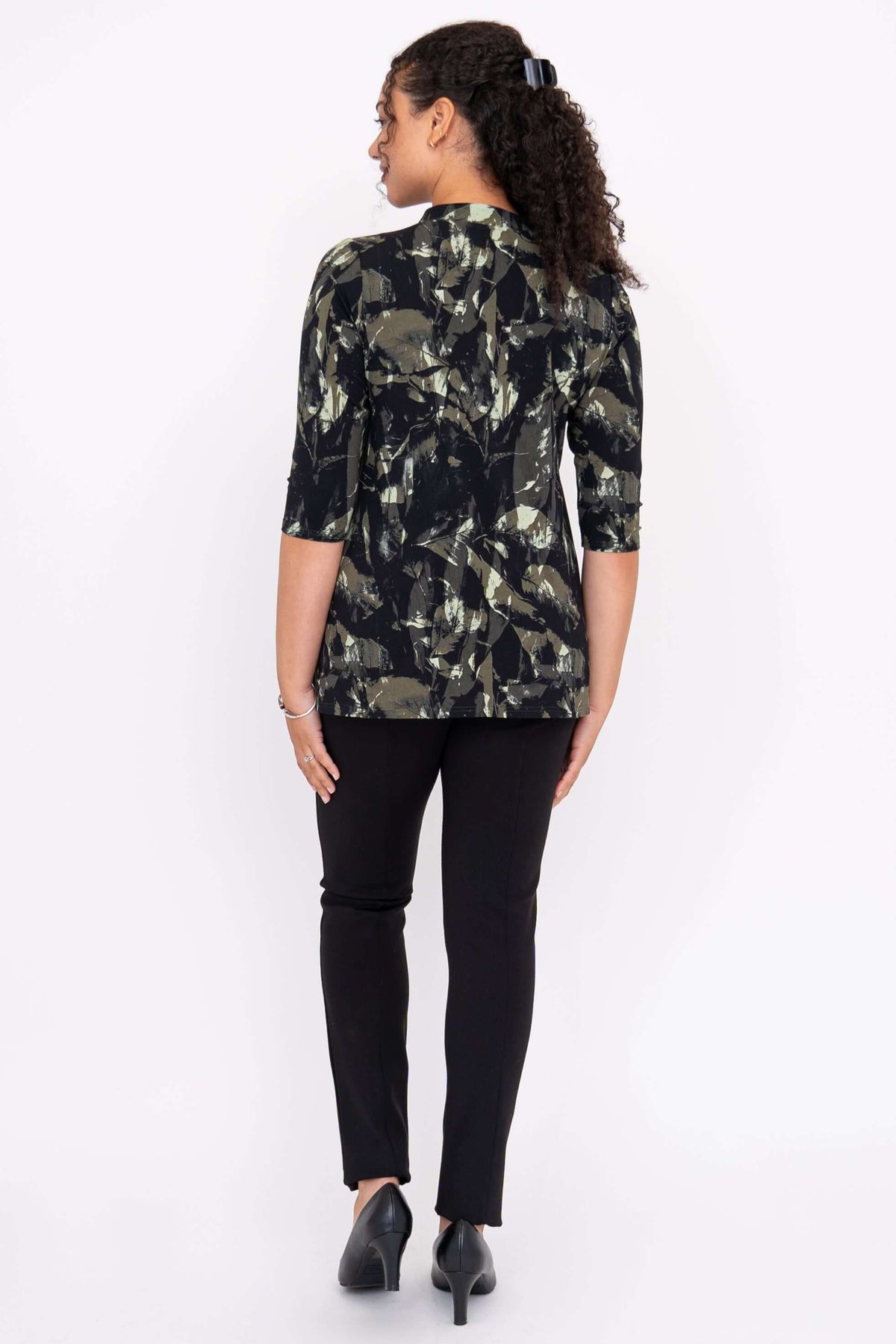 Back view of a woman wearing a black and green abstract pattern top and black pants