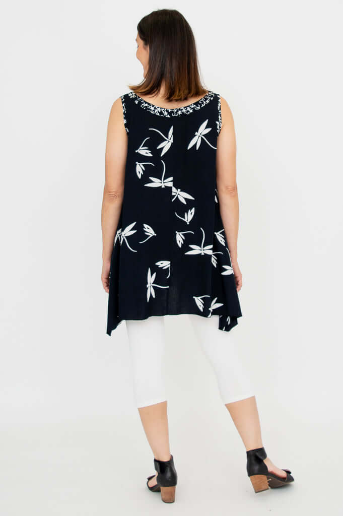 Back view of woman in sleeveless black tunic with white floral print and white leggings