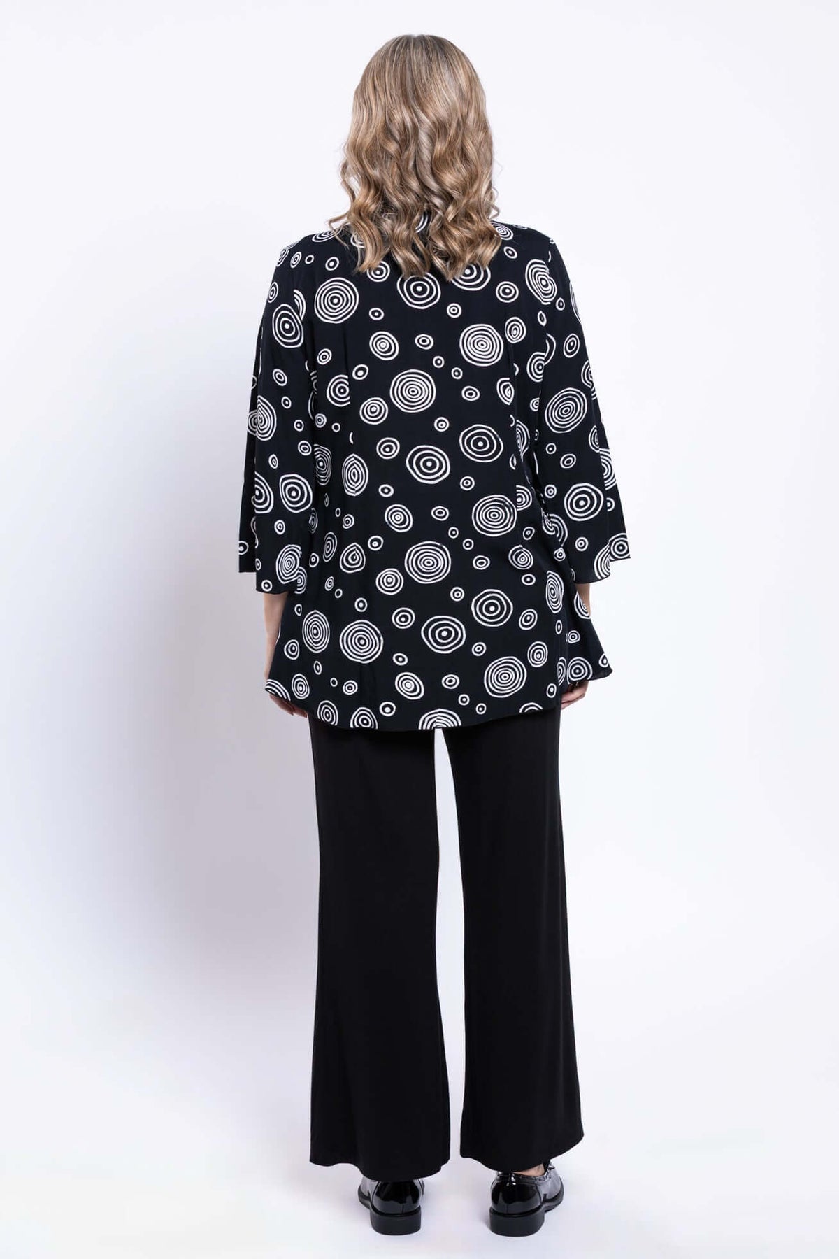 Back view of a woman wearing a black and white circle patterned blouse and black pants