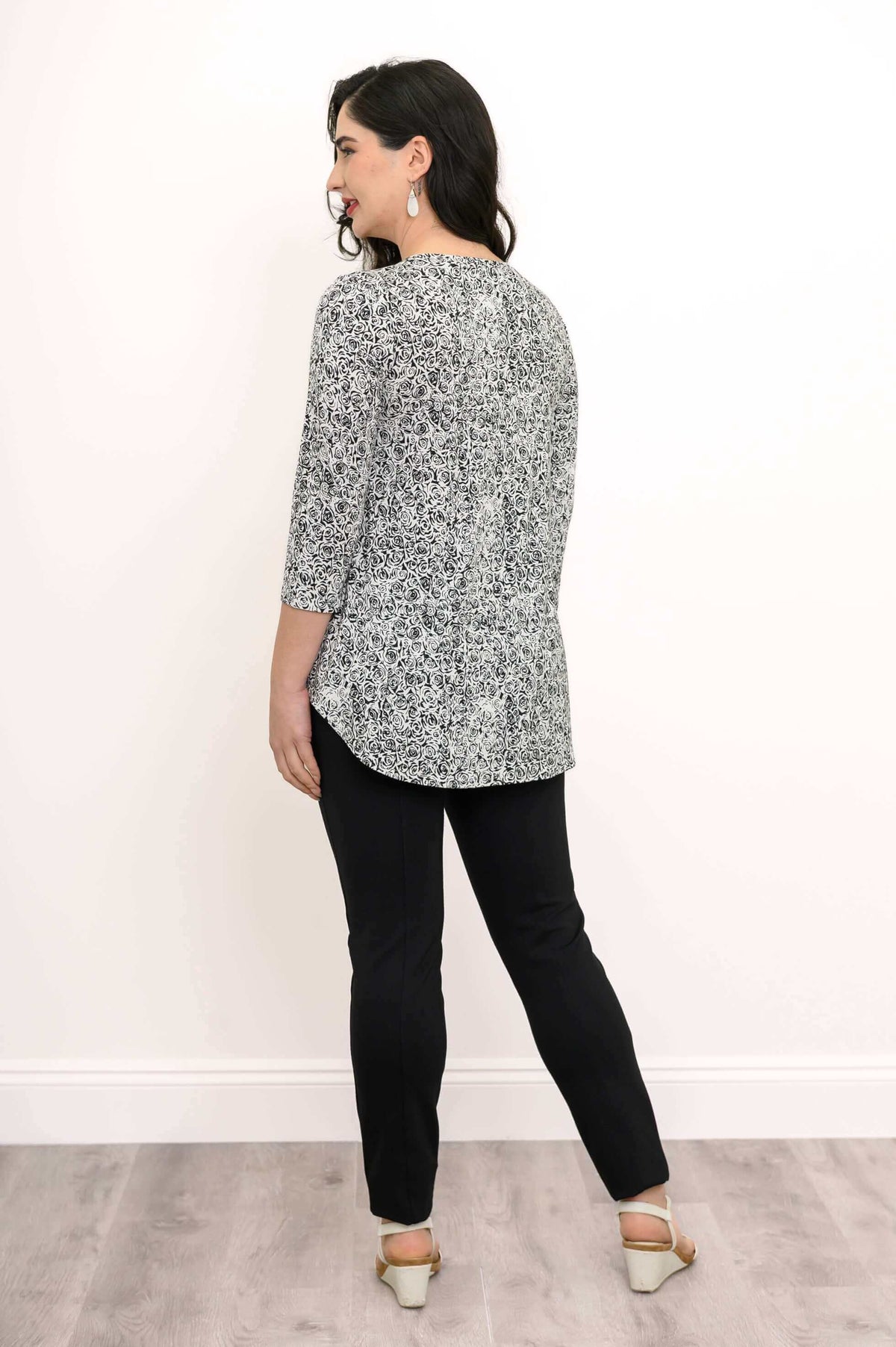 Back view of woman wearing black and white rose print top with curved hem